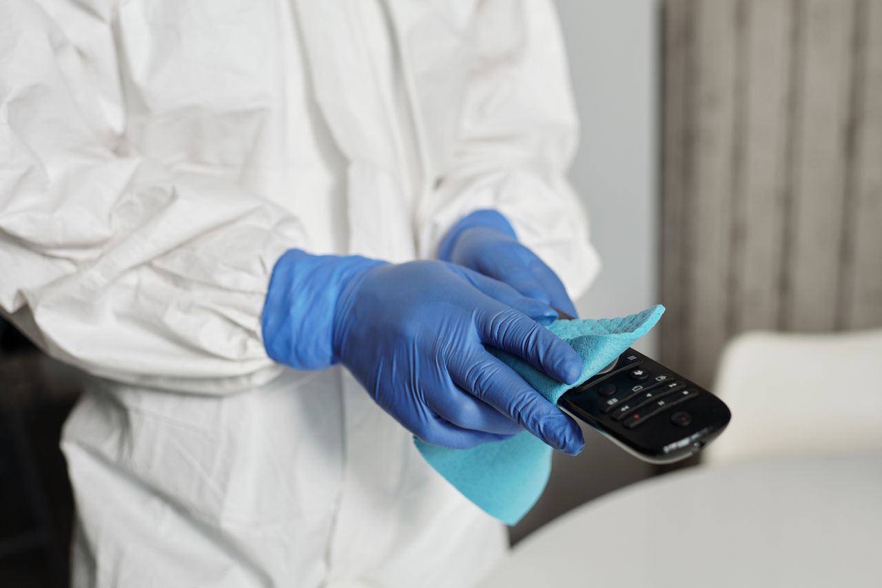 why-choose-us Close-up showing a person sanitizing a remote control while wearing protective gloves to keep it clean.